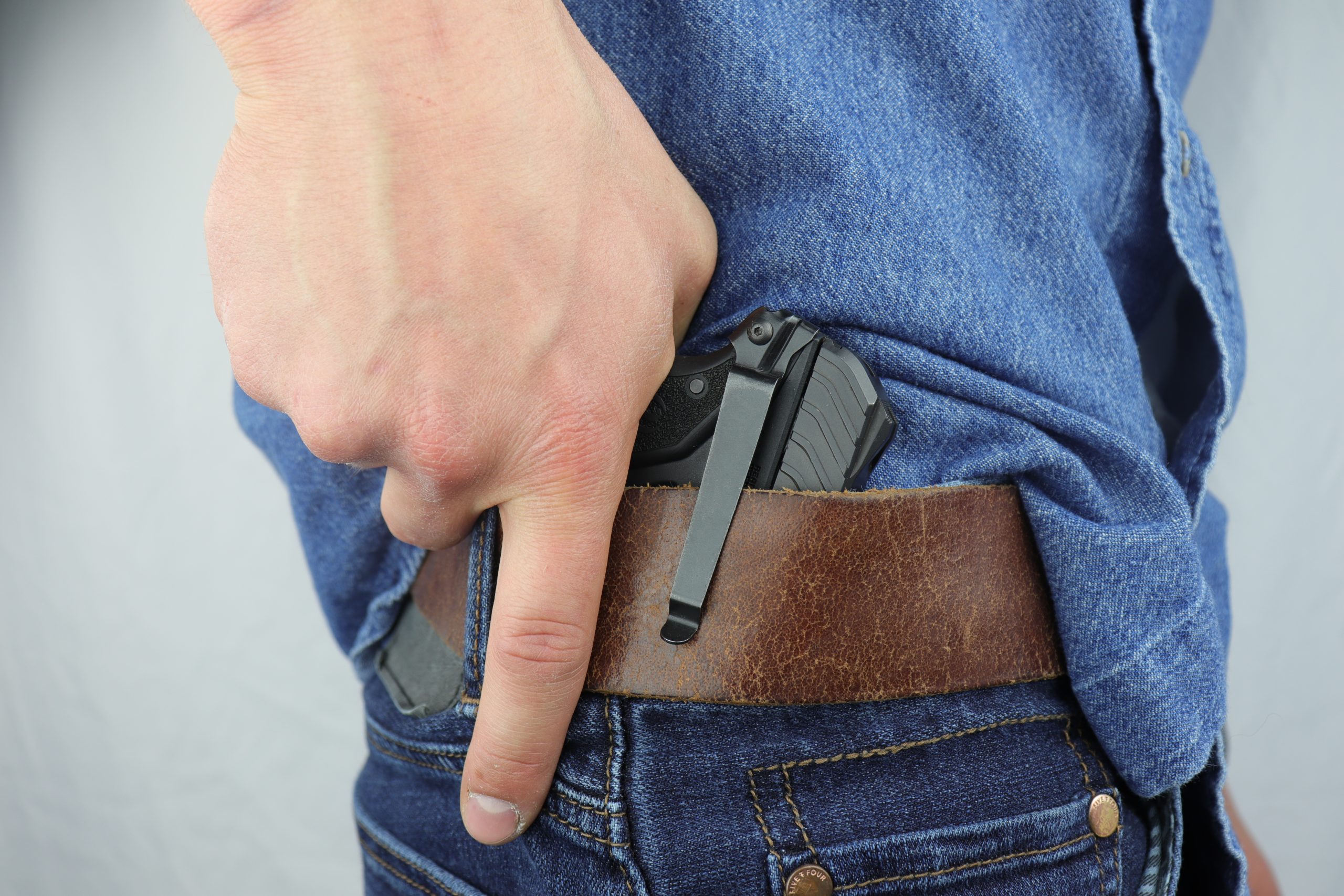 A person reaching for a pistol secured to their waistband with a Clipdraw belt clip.