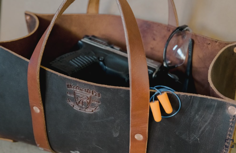 Leather Tool Shooting Bag Tote with a pistol, protective eyewear, and earplugs stored in its roomy main compartment.